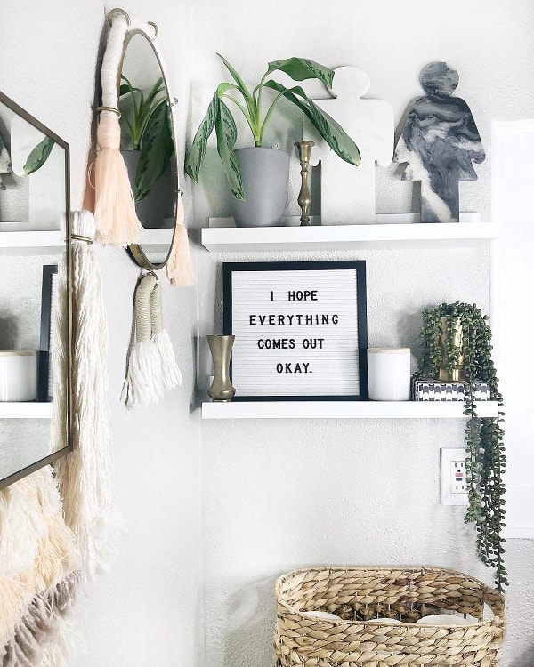 Boho bathroom shelf with plant, letter board, candles, and decorative accents.