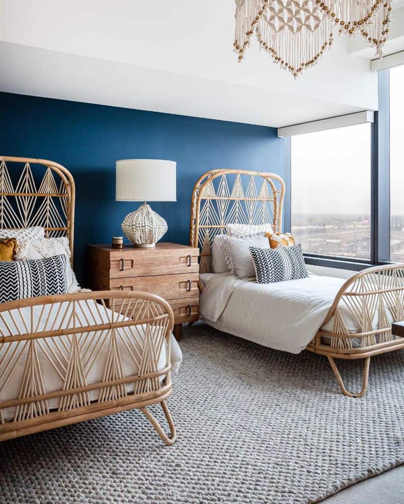 Modern boho bedroom with twin rattan beds, deep blue accent wall, and textured rug.