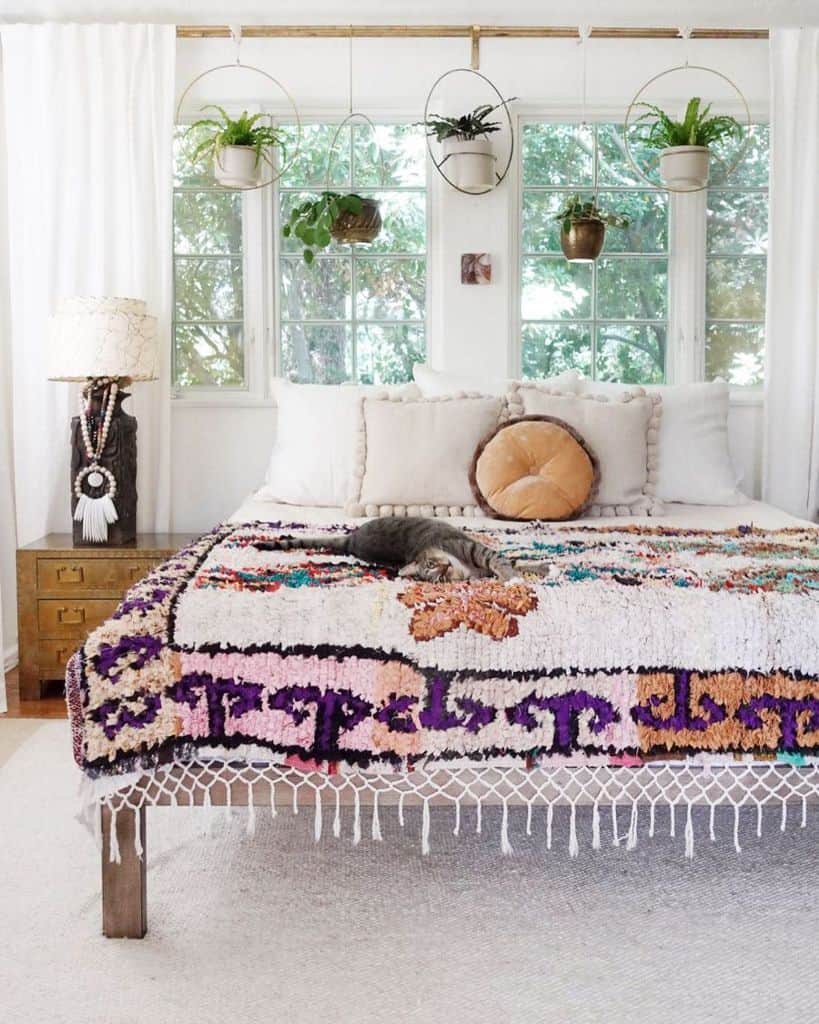 Boho bedroom with colorful textured bedding, hanging plants, and cozy natural light ambiance.