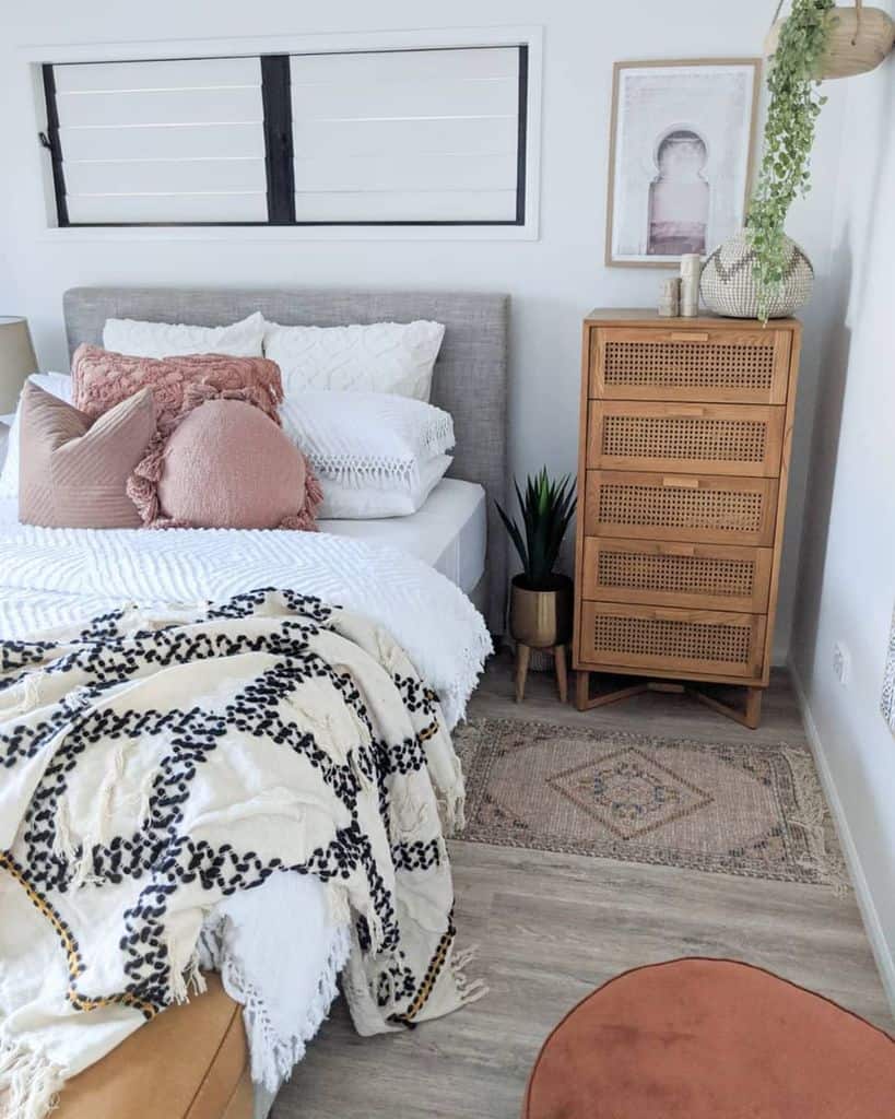 Modern boho bedroom with textured bedding, wooden dresser, soft pink accents, and hanging greenery.