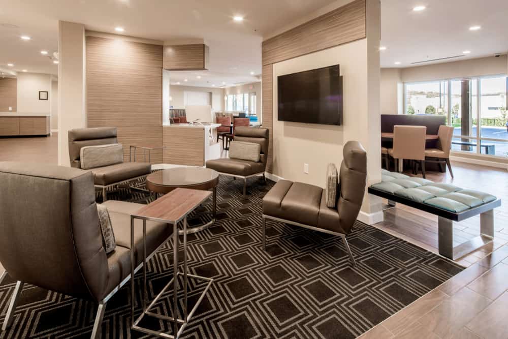 Modern hotel lobby with stylish brown seating, geometric rug, and a wall-mounted TV. Bright and inviting ambiance