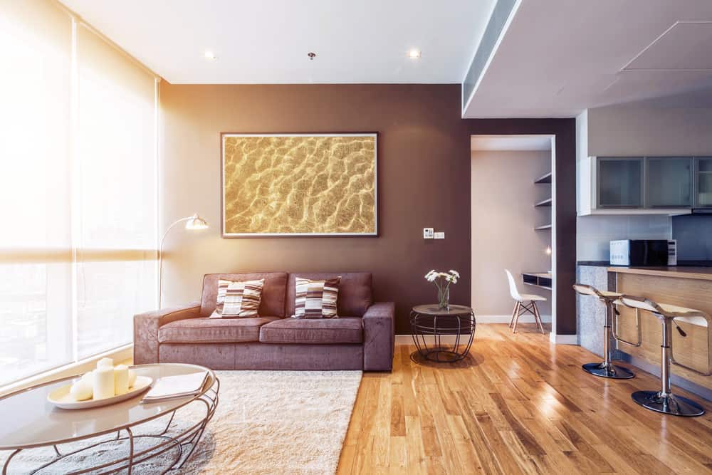 Modern living room with a cozy brown sofa, abstract art, wooden floor, and kitchen area