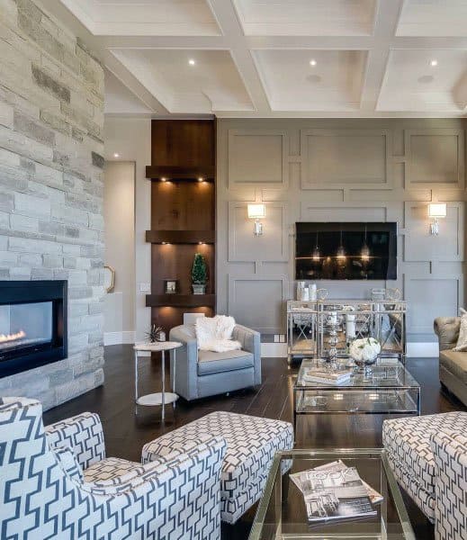 Modern living room with stone fireplace, coffered ceiling, patterned chairs, and a large TV above a console table