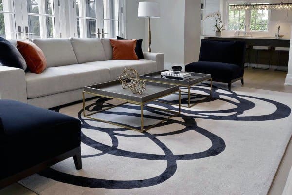 Modern living room with gray sofa, black chairs, geometric rug, and glass table; large windows illuminate the space