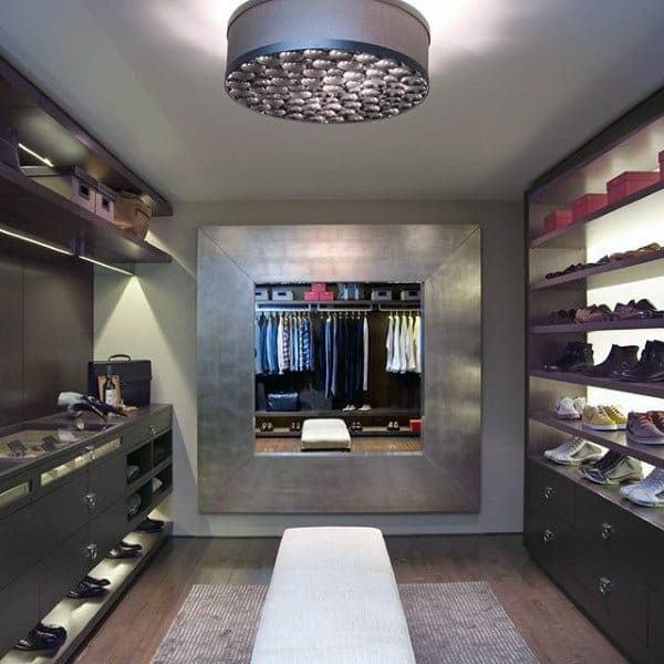 Modern closet with a large mirror, shoe shelves, clothes racks, and a central bench under a stylish light fixture