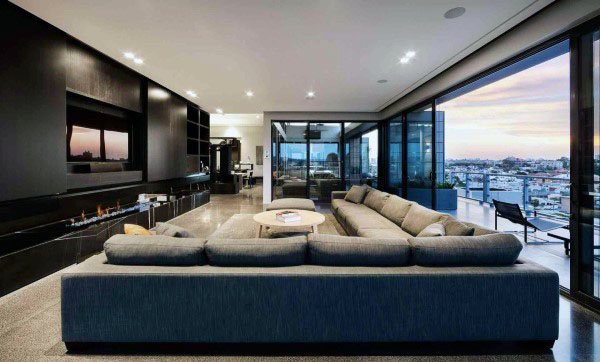 Modern living room featuring a large gray sectional sofa, sleek black walls, and city views through expansive windows