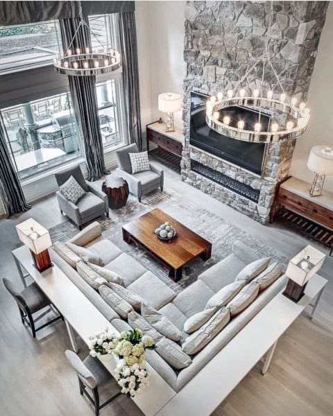 Spacious living room featuring a grey sectional sofa, stone fireplace, large windows, and elegant modern chandeliers