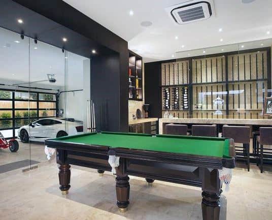 Modern garage bar with a billiard table, sleek bar setup, and glass wall showcasing a luxury car.