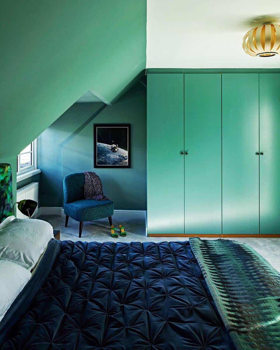 Green-themed bedroom with a large wardrobe, upholstered chair, and bed with dark bedding under sloped ceiling