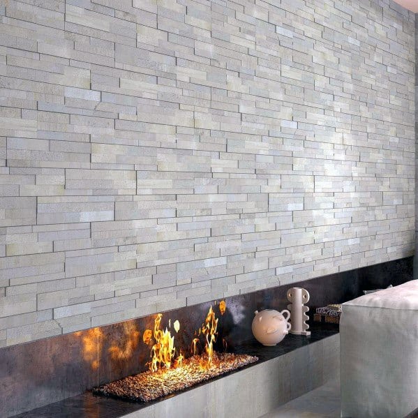 A sleek linear fireplace set against a textured grey stacked stone wall, creating a modern, cozy ambiance.