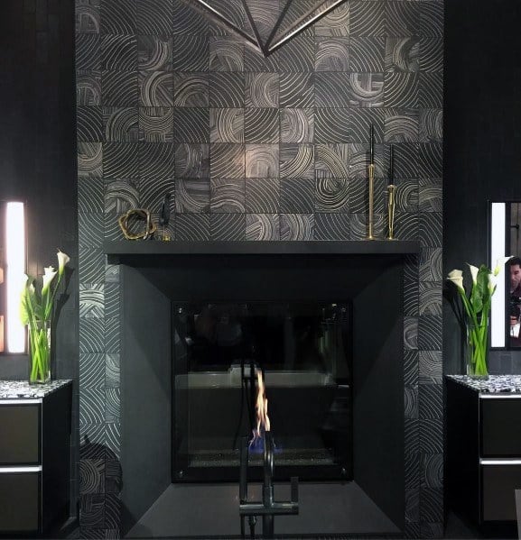 A sleek fireplace with modern gray tiles featuring intricate patterns, complemented by a minimalist black mantel and elegant decor.