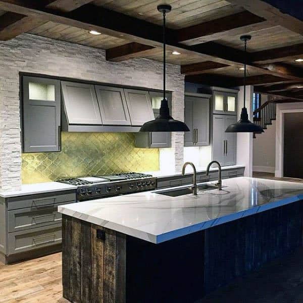 Rustic kitchen with marble island, gray cabinets, wood beams, and industrial pendant lights.