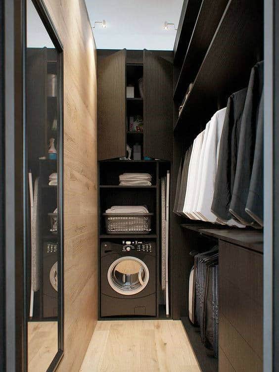 Compact laundry room with a washing machine, shelves of folded clothes, and a wooden floor