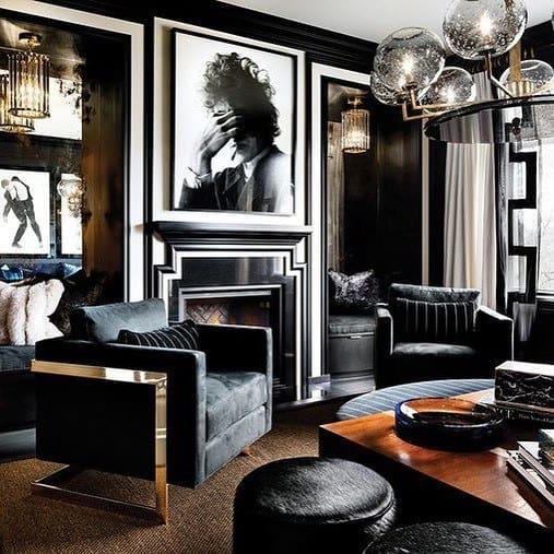 Elegant black living room featuring velvet chairs, modern lighting, and a large portrait above the fireplace