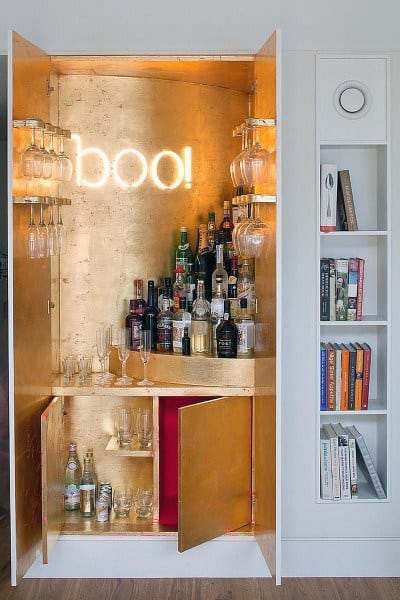 Gold-accented mini bar with a neon "boo!" sign, glass racks, and a stylish display of bottles.