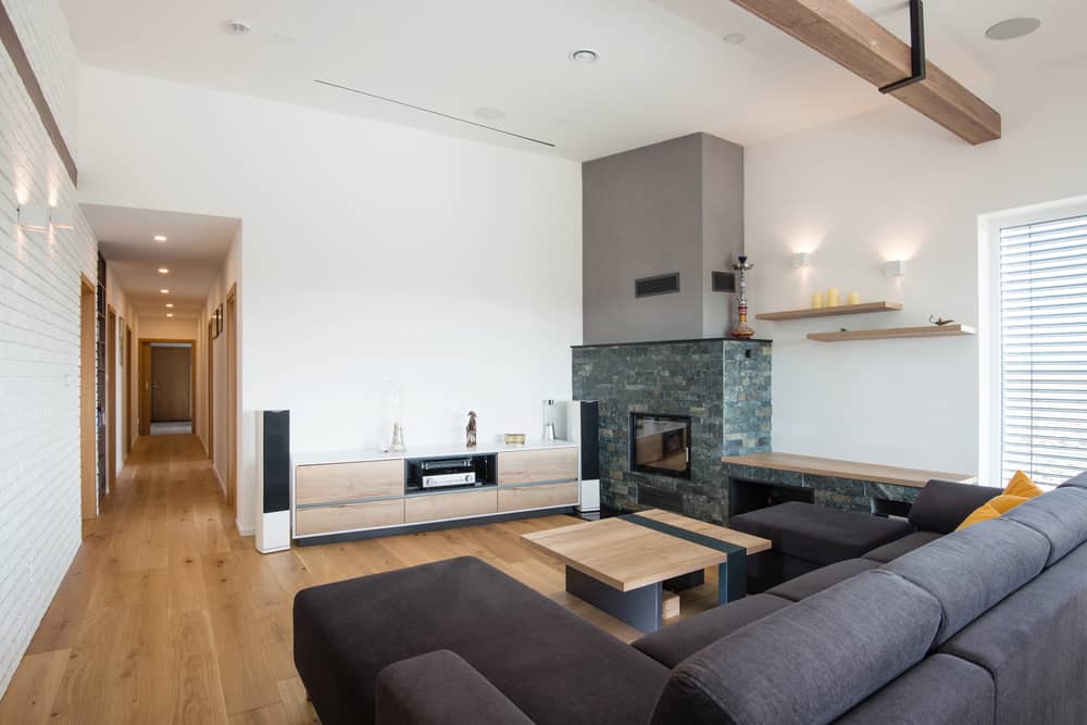 Contemporary living room with a gray sectional sofa, stone fireplace, wooden accents, and a bright, open layout