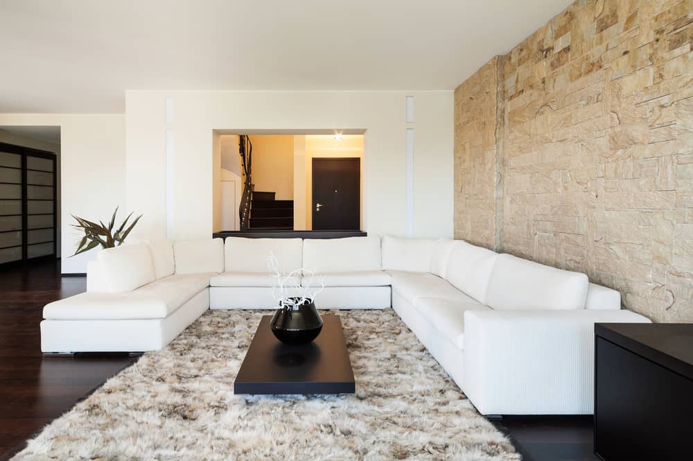 Modern living room with a white sectional sofa, textured stone accent wall, shag rug, and sleek black coffee table