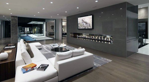 Modern living room featuring white sofas, a sleek fireplace, TV, and large glass doors leading to a lit pool area