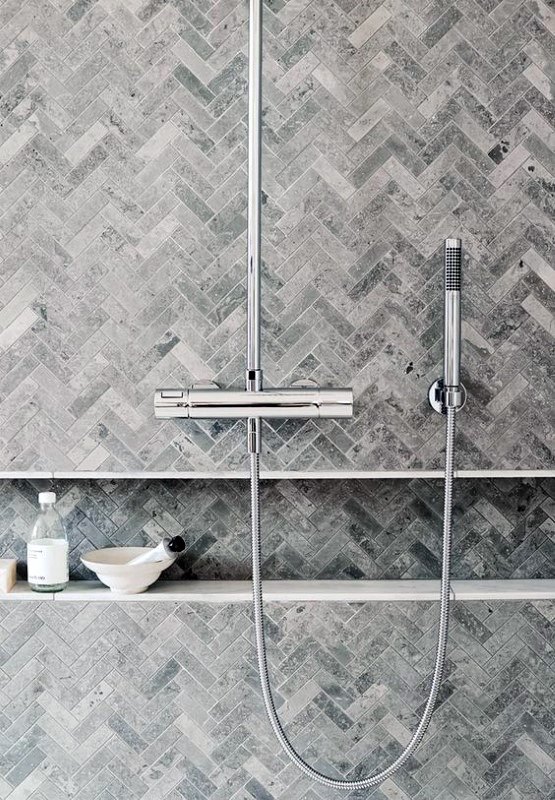 Shower with gray herringbone tiles, sleek chrome fixtures, and recessed shelf for toiletries.