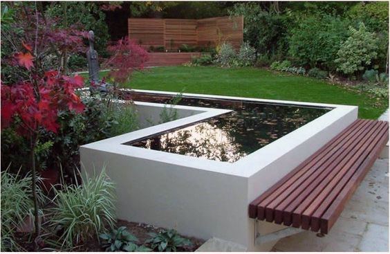 Raised concrete pond with clean lines, a built-in wooden bench, and surrounded by lush garden plants.