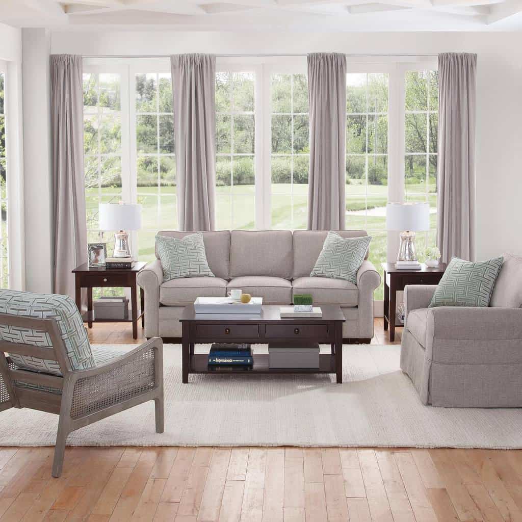 Elegant modern sunroom featuring a neutral gray sofa set with matching armchairs, soft drapes, and a wooden coffee table.