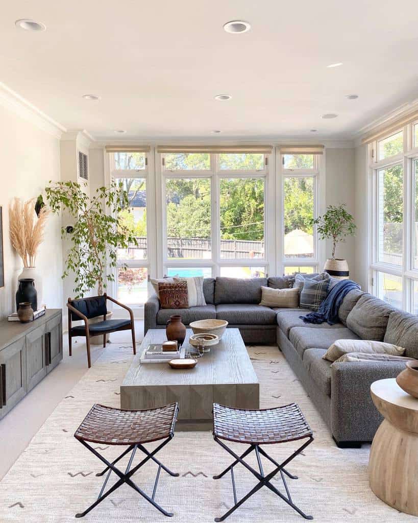 Modern sunroom with a gray sectional, leather stools, and a rustic coffee table.