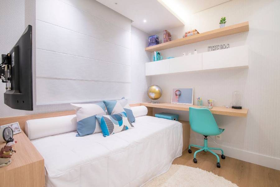 Small modern bedroom with wall shelves, turquoise chair, mounted TV, and a sleek workspace.