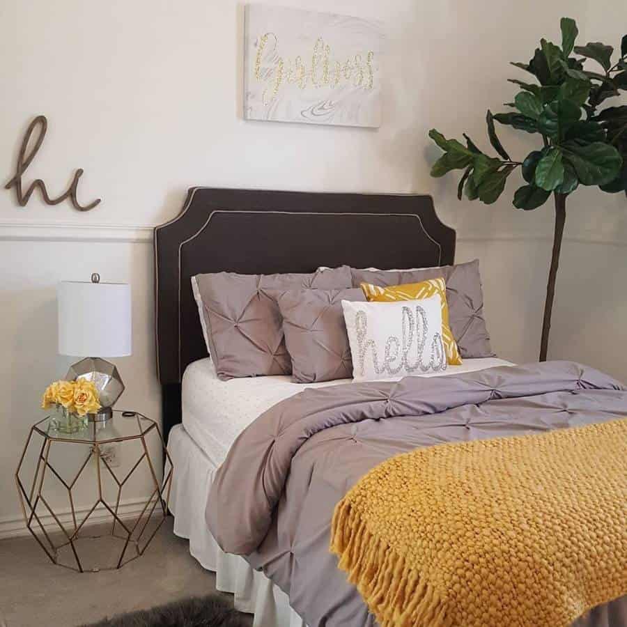 Cozy bedroom with grey bedding, yellow accents, and decorative pillows on a tufted bed.