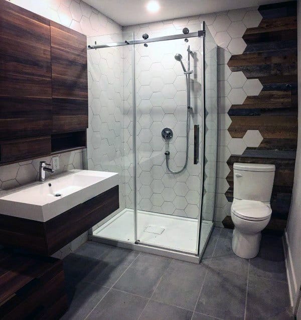 Modern bathroom with hexagonal white tiles, glass shower, and wood accent wall.