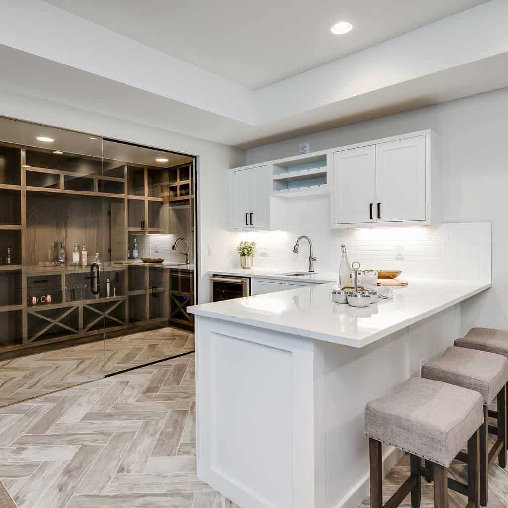 Minimalist wet bar with white cabinetry, quartz countertops, and adjacent glass-enclosed wine room.