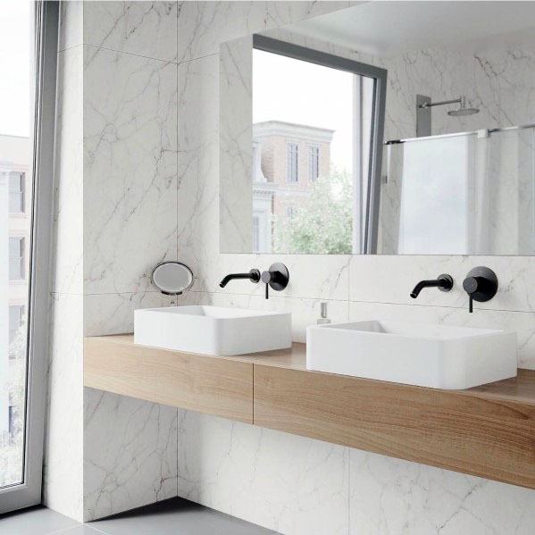 Modern bathroom with white marble walls, floating wood vanity, and double sinks.