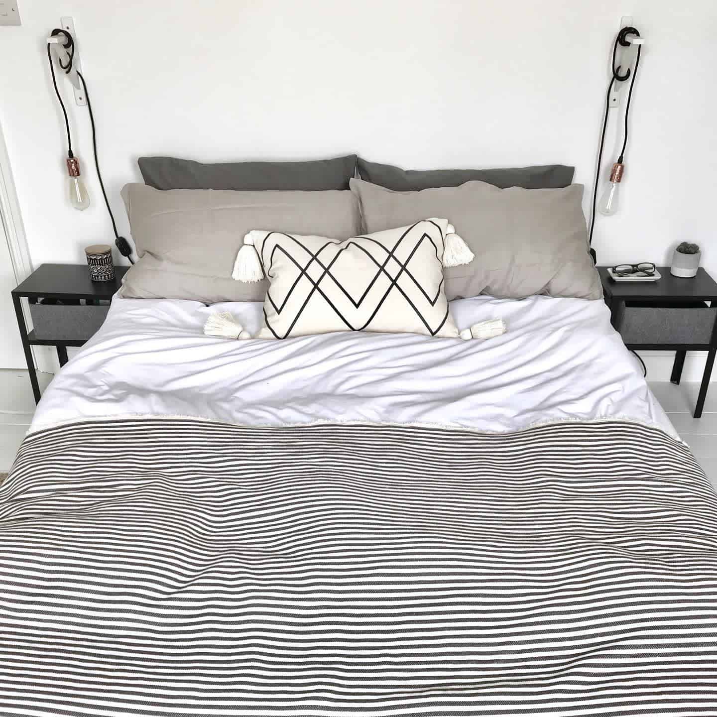 Minimalist bedroom with a striped bedspread, black nightstands, and exposed globe lights.