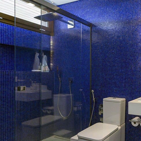 Modern bathroom with small blue mosaic tiles, glass shower, and white fixtures.