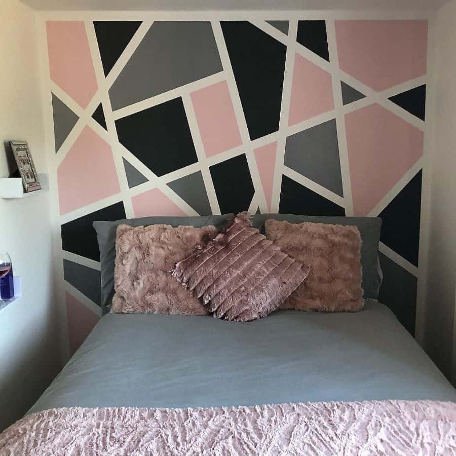 Small bedroom with pink, gray, and black geometric feature wall and plush pillows.