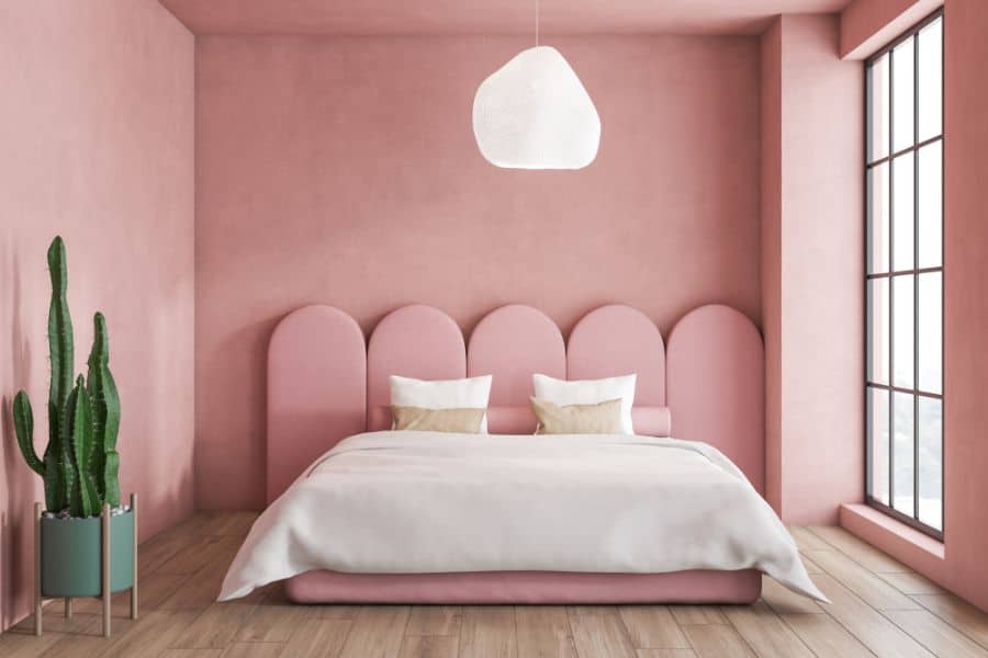 Muted pink bedroom with floorboards, a minimalist cactus in a pot, and an arched headboard design.