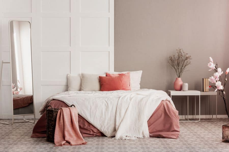 Muted-tone bedroom with tall mirror, blush accents, and floral decor on side table.