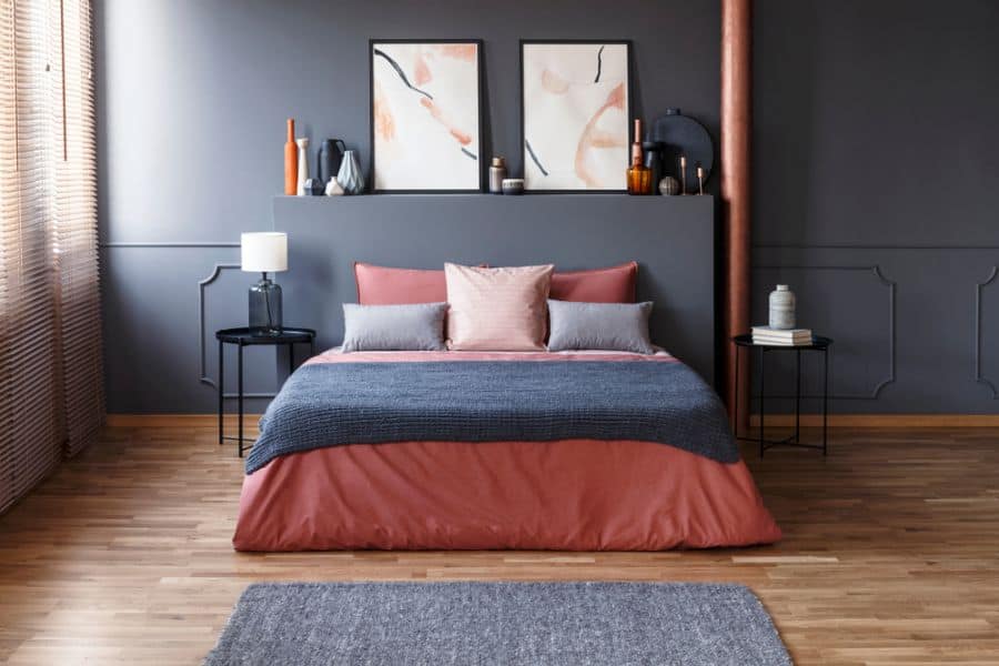 Modern bedroom with dark gray walls, pink bedding, wood floors, and abstract wall art.