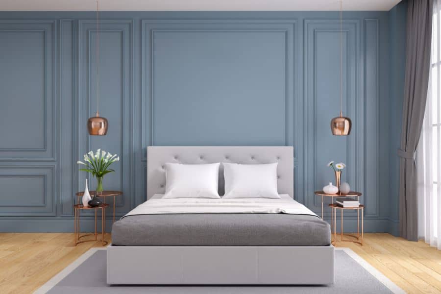 Blue bedroom with tufted gray bed, bronze bedside tables, and matching pendant lights.