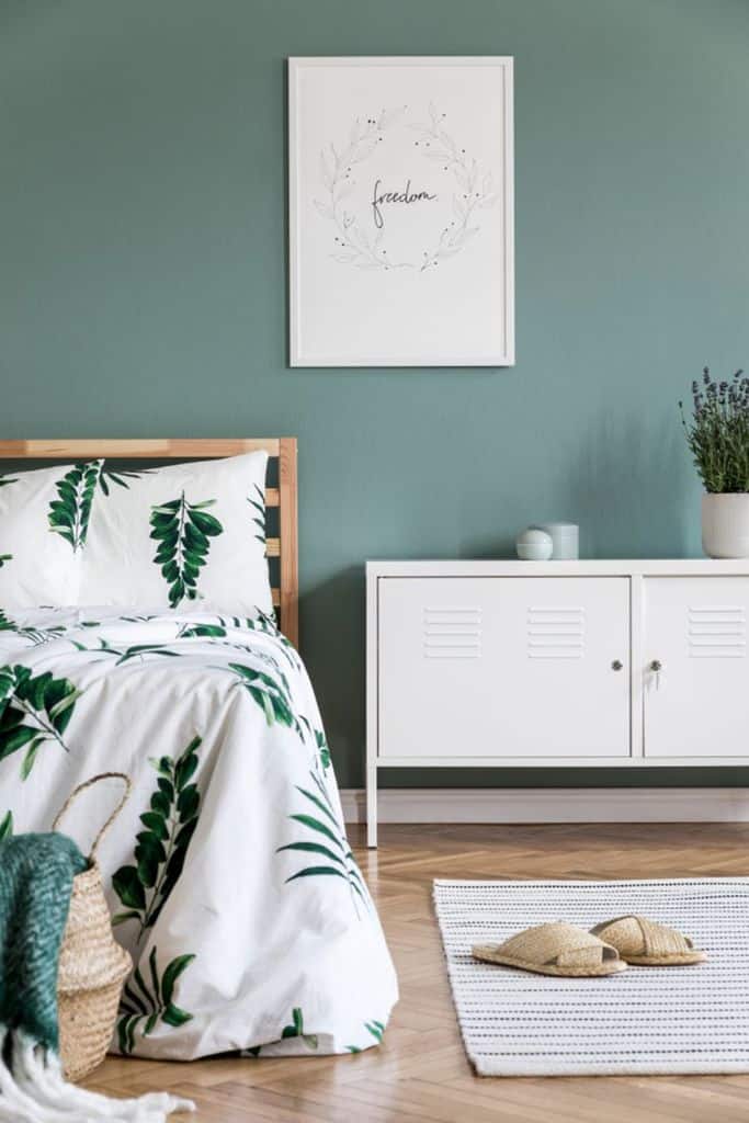 Green bedroom with botanical bedding, white cabinet, and “freedom” wall art.