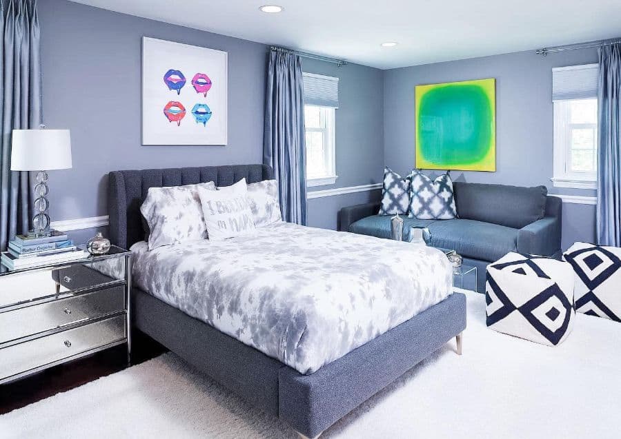 Modern gray bedroom with tufted bed, mirrored nightstand, couch, and vibrant wall art.