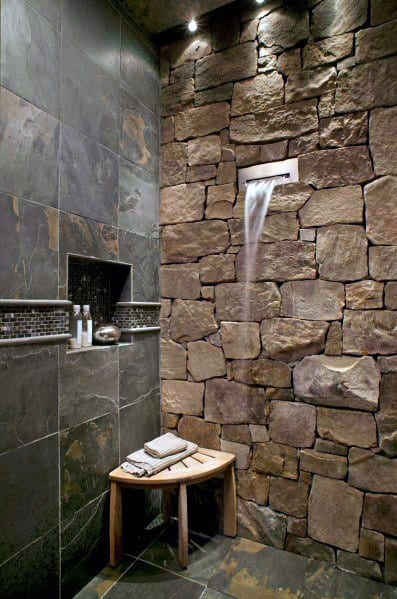 Rustic stone wall shower with waterfall faucet and built-in shelf.