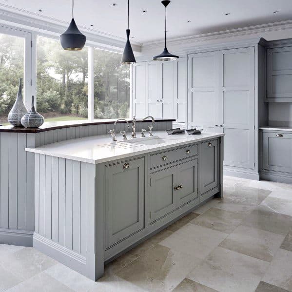 This kitchen features soft grey cabinetry with sleek natural stone flooring, creating a spacious, modern ambiance with ample natural light