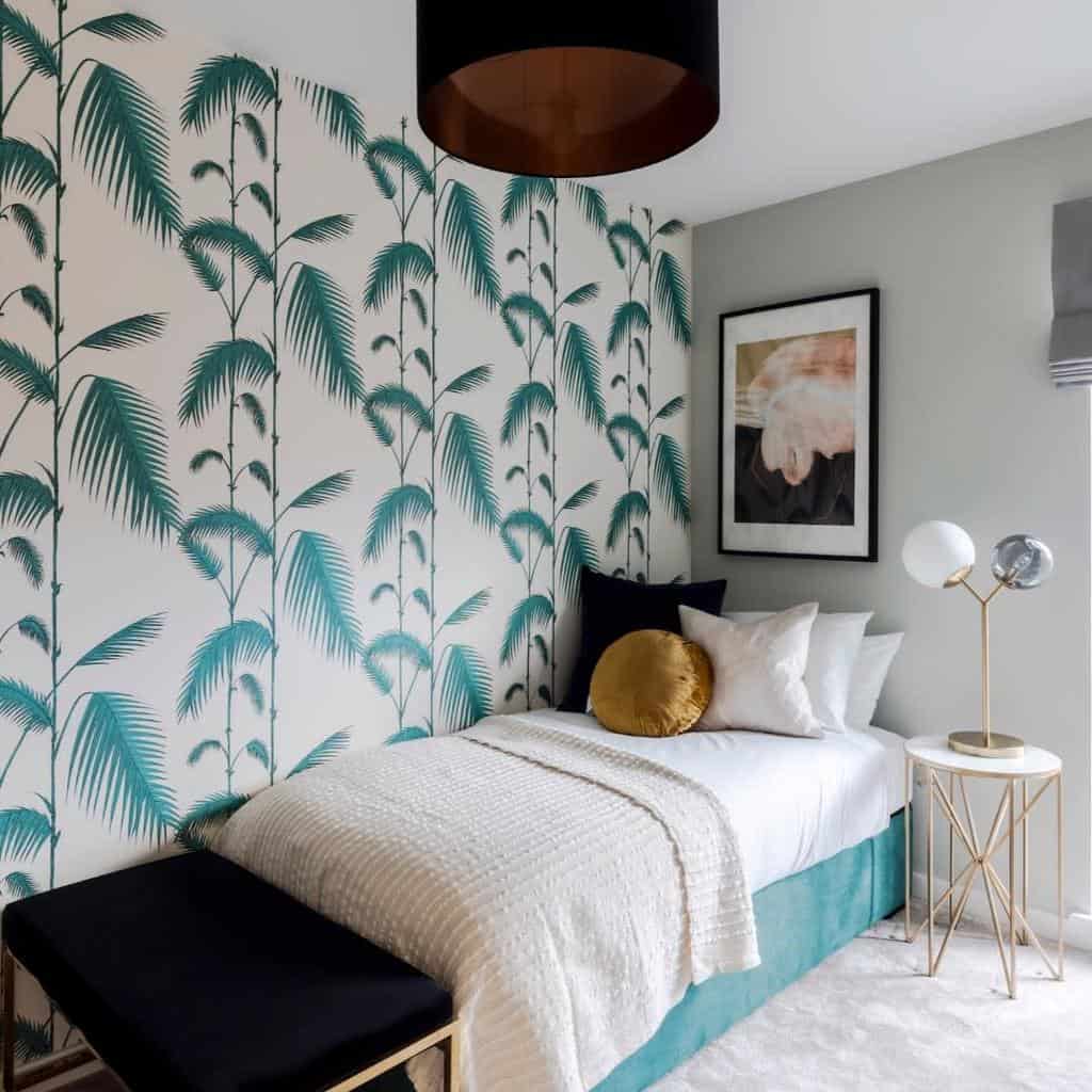 Small bedroom with fern wallpaper, teal bed, and framed wall art above a side table.