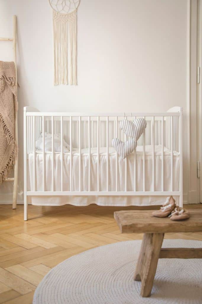 Boho baby room with white crib, macramé wall hanging, and soft neutral tones on hardwood flooring.