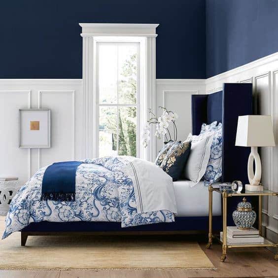 Bright navy and white bedroom with patterned bedding, wingback bed, and elegant side table.