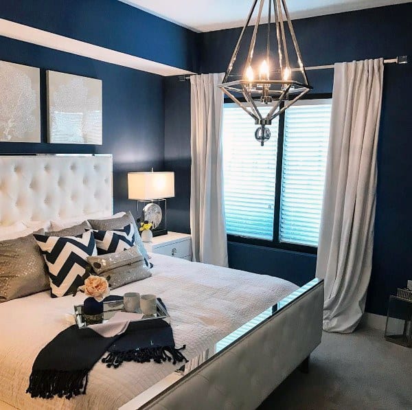 Navy bedroom with tufted white bed, chevron pillows, and a modern chandelier.