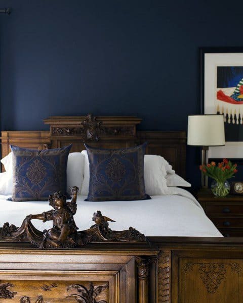 Classic navy bedroom with ornate wooden bed frame, patterned pillows, and elegant decor.