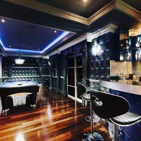 Luxurious game room with pool table, bar area, glossy wood floors, and navy blue decor.