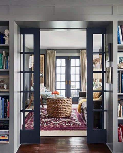 Navy blue pocket doors with glass panels open to a cozy living room featuring a red patterned rug, wicker table, and French doors