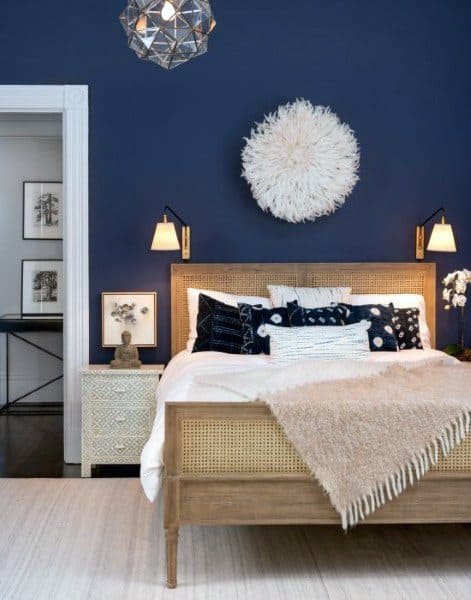 Bedroom with navy blue walls, rattan bed frame, layered throw pillows, and cozy beige blanket.